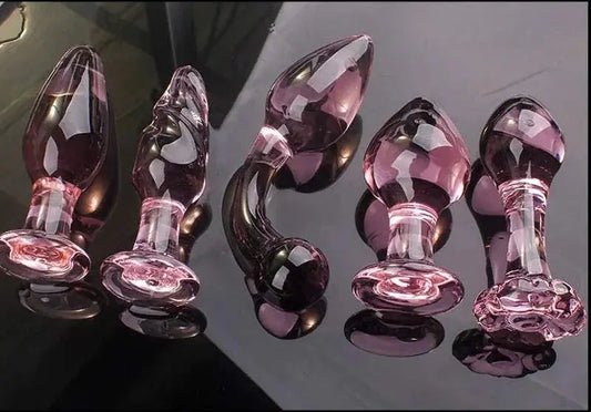 Candiway pink crystal glass anal plugs in various styles on black surface.