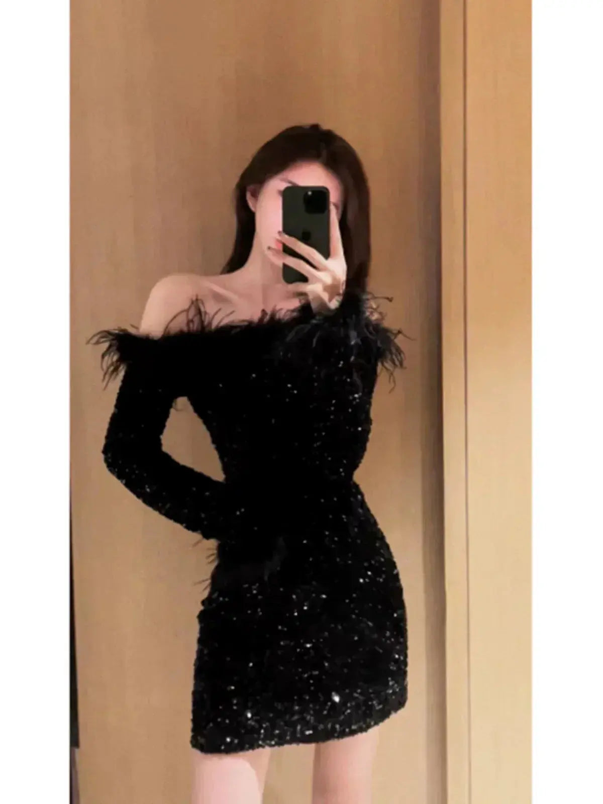Woman wearing black shoulder sequin sexy dress with long sleeves and feather details taking mirror selfie