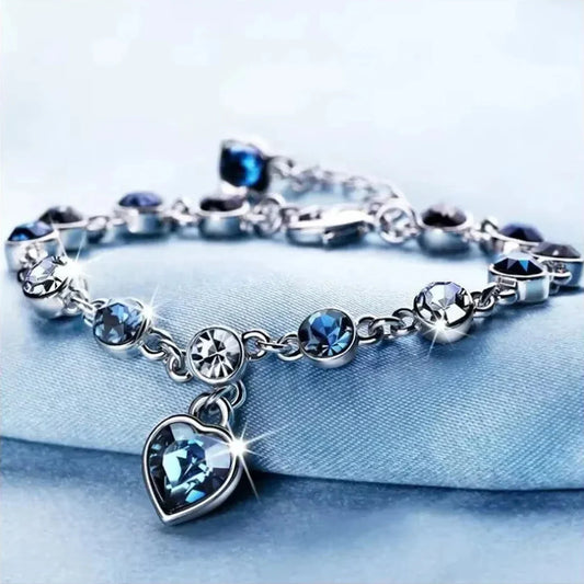 Women silver color lucky bracelet with blue crystal heart charm on blue background