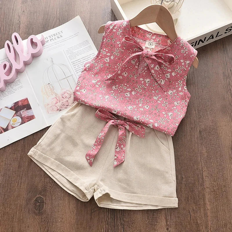 Summer baby girls sleeveless floral pink vest with beige shorts set on wooden background