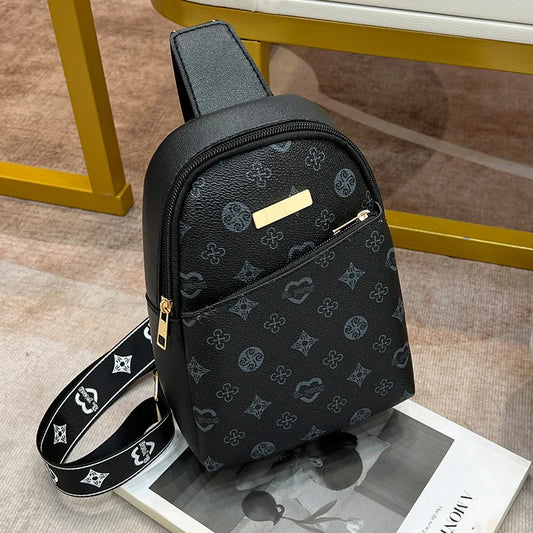 Black women's crossbody chest bag with printed design and adjustable strap placed on a magazine and carpeted floor.