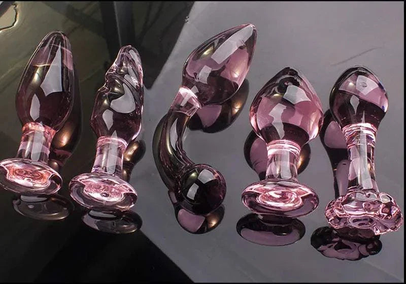 Candiway pink crystal glass anal plugs in various styles on black surface.