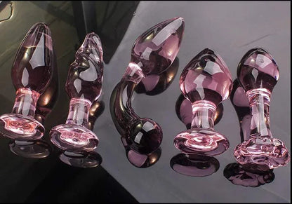 Candiway pink crystal glass anal plugs in various styles on black surface.