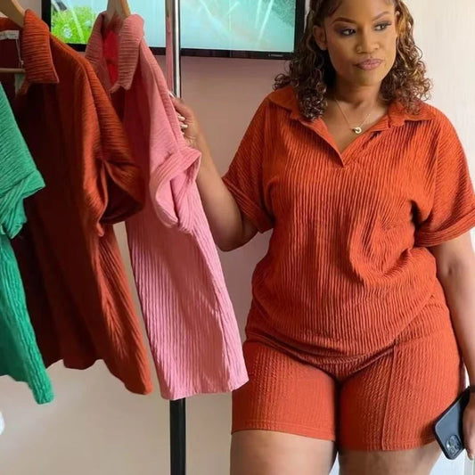 Woman wearing rust orange casual two-piece set with short sleeves and shorts holding matching tops in multiple colors hanging on rack