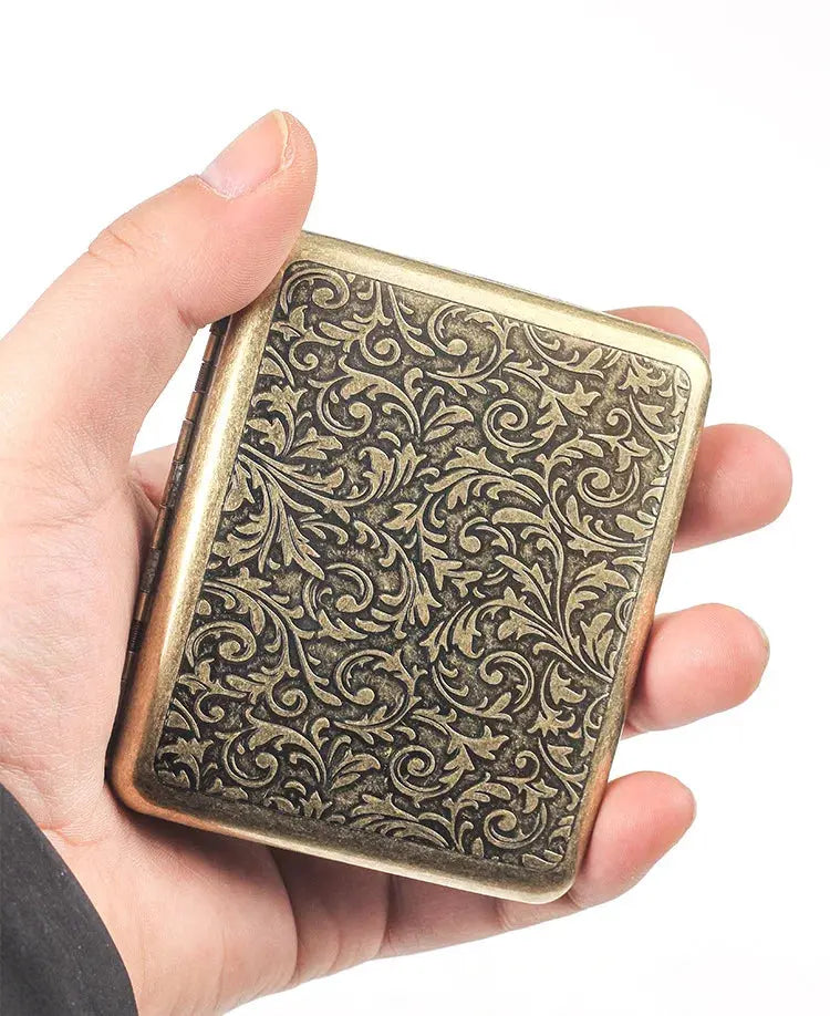 Retro cigarette box with frosted brass design, held in hand.