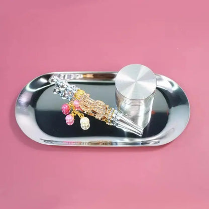 Metal rolling tray with spice grinder and smoking accessories set on pink background.