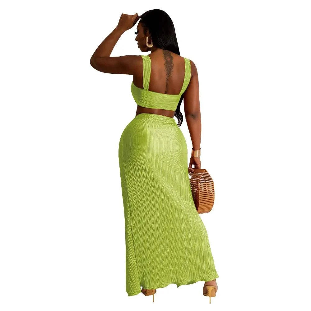Back view of a woman wearing a green summer two-piece set with a backless halter top and high waist side slit pleated skirt suitable for beach streetwear fashion.