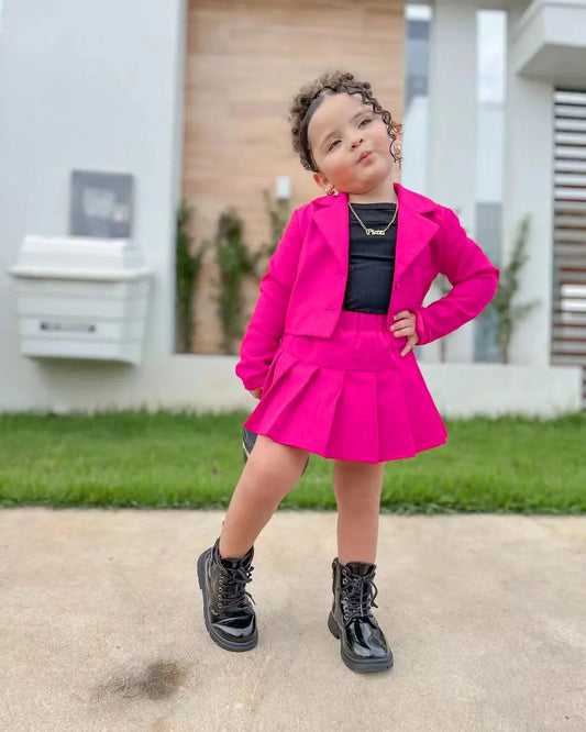 toddler girl wearing bright pink button front jacket and skirt set with black top and boots outdoors spring autumn outfit