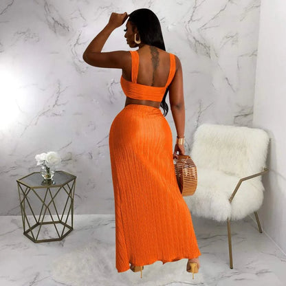 Two-piece orange dress set with a backless halter top and high waist side slit pleated skirt on a woman.