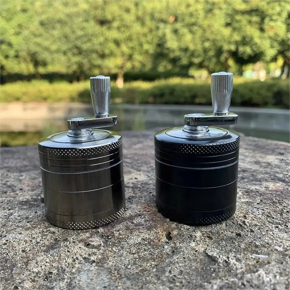 4-layer zinc alloy herbal grinders in black and silver with crank handles on a stone surface.