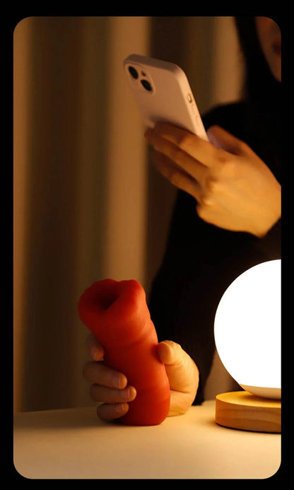 Men's automatic tongue licking oral sex toy in red, handheld next to a lamp.