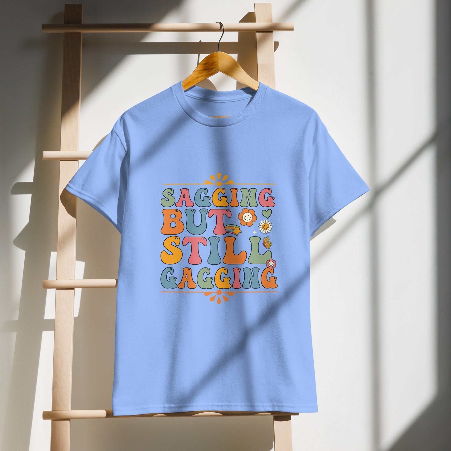 Saggin Still Gaggin DryBlend® T-Shirt hanging on a wooden ladder in sunlight.