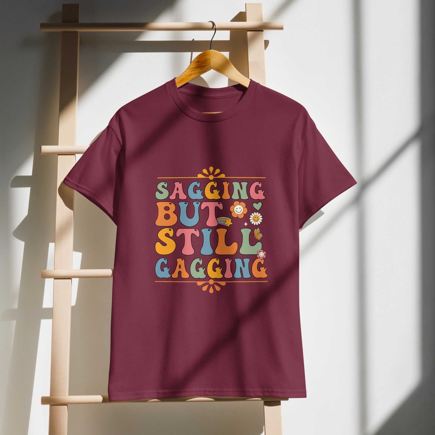 Saggin Still Gaggin DryBlend T-Shirt hanging on wooden ladder, modern classic fit, moisture-management fabric.