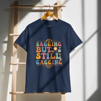 Saggin Still Gaggin DryBlend® T-Shirt hanging on a wooden rack, showcasing vibrant design and modern classic fit.